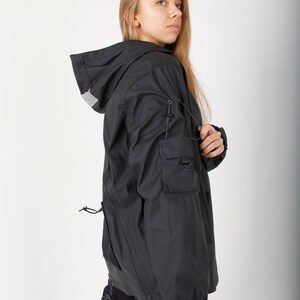 May include: A black hooded jacket with a drawstring waist and a reflective detail on the hood. The jacket has a zipper closure and a large pocket on the left sleeve.