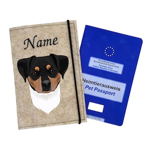 Könnte beinhalten: Ein beigefarbener Filz-Reisepasshalter mit einer Illustration eines schwarz-weißen Hundes. Der Halter hat ein schwarzes Gummiband und den Text "Name" vorne aufgestickt. Der Halter befindet sich neben einem blauen EU-Heimtierausweis mit dem Text "Heimtierausweis Pet Passport" und der Nummer "05 1119102".