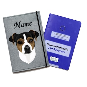 Könnte beinhalten: Ein grauer Filz-Reisepass-Etui mit einem schwarzen Gummiband und einer Illustration eines weißen und schwarzen Hundes. Der Text "Name" ist auf der Vorderseite gestickt. Das Etui liegt neben einem blauen Heimtierausweis mit dem Text "Heimtierausweis Pet Passport" und dem Logo der Europäischen Union.