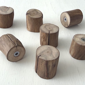 May include: Seven small, cylindrical wooden holders with a natural wood grain finish. Each holder has a slot cut into the top and a metal insert in the base. The holders are arranged on a white surface.