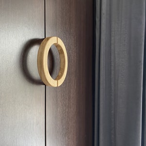 May include: A wooden door handle with a circular design. The handle is light brown and has a smooth finish. The door is a dark brown wood.