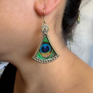 May include: Gold tone earrings with a peacock feather design. The earrings are shaped like a teardrop and have a beaded border.
