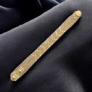 Peut inclure: Un bracelet doré doté d'une construction en maille fine avec une surface texturée. Le bracelet comprend deux accents décoratifs circulaires à une extrémité et un fermoir lisse et arrondi de style bouton à l'autre extrémité de la bande.