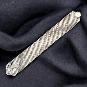 Peut inclure: Un bracelet argenté doté d'une structure en maille fine et texturée avec un éclat métallique. La bande rectangulaire est fixée par deux boutons-pression circulaires et gaufrés à une extrémité et un seul bouton-pression assorti à l'autre.