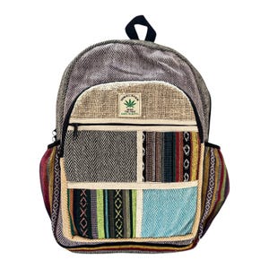 Può includere: Zaino multicolore con una varietà di pannelli a motivi. Il corpo principale presenta un motivo a spina di pesce, con una tasca frontale con un design patchwork di strisce e forme geometriche. Il pannello superiore ha un logo a forma di foglia di canapa.