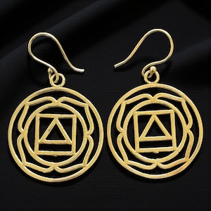 May include: A pair of gold-coloured earrings. Each earring features a circular design with a square and triangle shape in the centre, surrounded by a floral-like pattern. The earrings have a hook closure.
