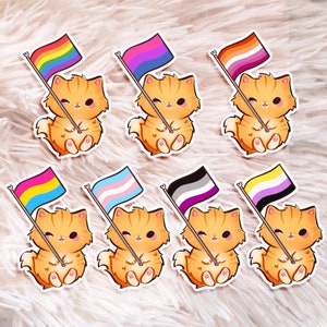 May include: Eight colorful pride flag stickers with orange tabby cats holding them. The flags are rainbow, transgender, bisexual, lesbian, pansexual, asexual, genderqueer, and non-binary.