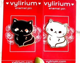 May include: Two enamel pins featuring a black cat and a white cat with gold accents. The pins are on red cards with the text "vylirium enamel pin" and "vylirium.com".