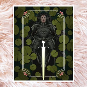 May include: A dark-haired woman in black armor stands with a sword in front of her. She has a third eye on her forehead and is surrounded by green lily pads.