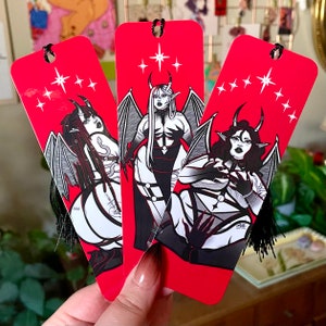 May include: Three red bookmark designs with black and white illustrations of women with wings and horns. The bookmarks have a red background with white stars and the text "666" on one of the bookmarks.