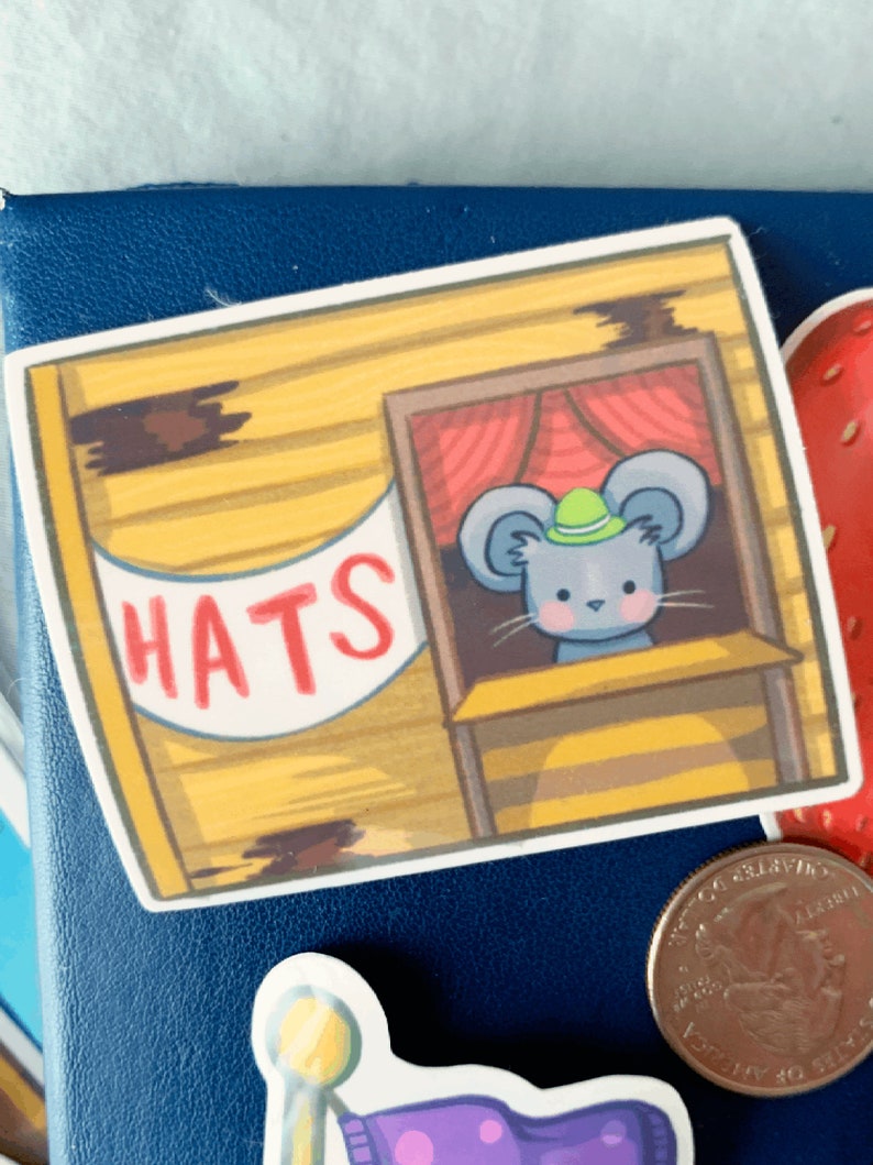 May include: A yellow and brown wooden shop with a red curtain and a sign that says "HATS". A grey mouse with a green hat is looking out of the shop window.