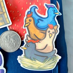 May include: A sticker featuring a stack of four cartoon birds. The bottom bird is blue, the next is brown, the next is white with a red comb, and the top bird is blue with a long, pointed beak. The birds are sitting on a bed of straw.