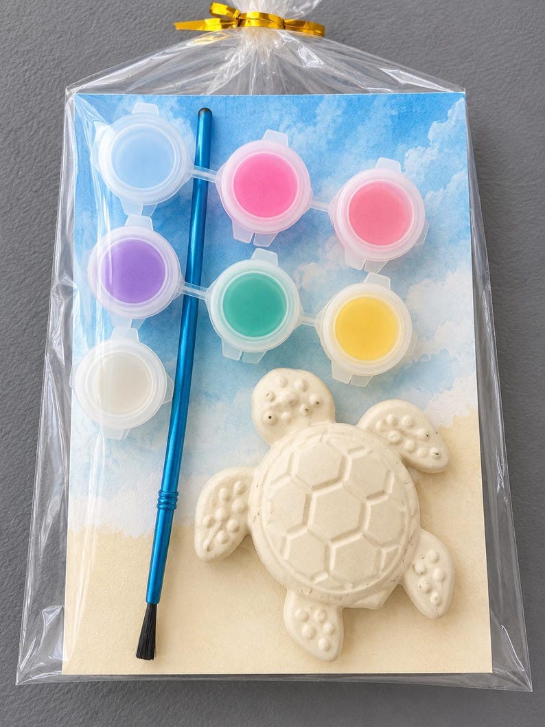 Puede incluir: Un kit de pintura de tortuga para pintar, empaquetado en celof&aacute;n transparente. El kit incluye una tortuga de cer&aacute;mica, un pincel azul y seis botes de pintura de varios colores. El fondo presenta una escena de playa con un cielo azul.