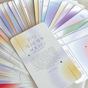 May include: A set of oracle cards with a pastel rainbow gradient background. The top card features the text "It's Already Yours" in black and white lettering. The text on the card reads "I am a clear receiver. I ground myself extending roots into the ground below, opening my crown to connect with Source. I intend my clairs are boosted to clearly hear, feel, see, and know. I intend to receive information for the highest good. I ask for assistance from Source for the clearest connection and information flow. I am thankful for this opportunity." The text is attributed to "madison england".
