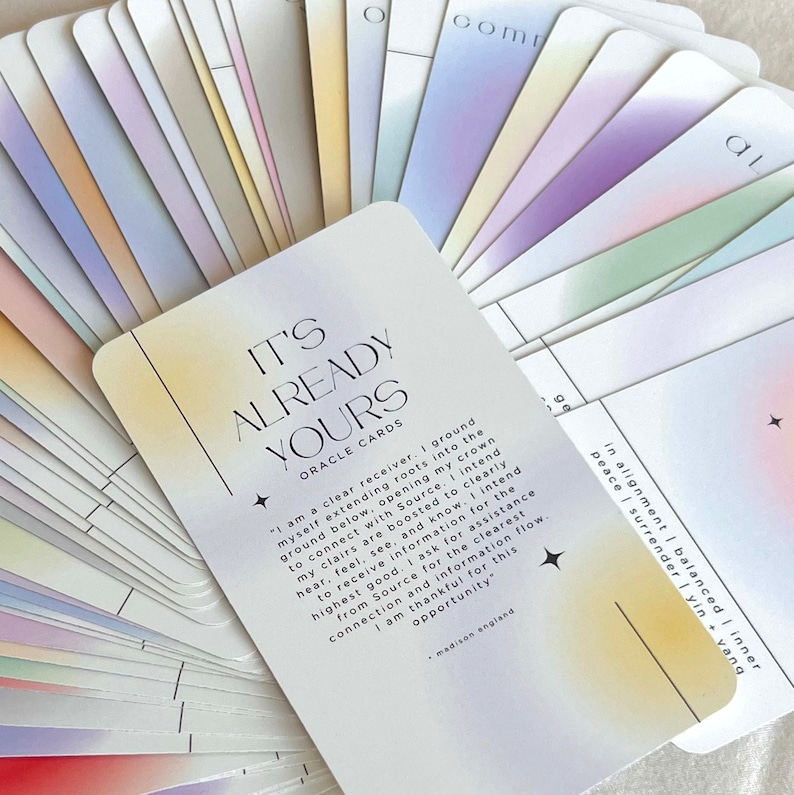May include: A set of oracle cards with a pastel rainbow gradient background. The top card features the text "It's Already Yours" in black and white lettering. The text on the card reads "I am a clear receiver. I ground myself extending roots into the ground below, opening my crown to connect with Source. I intend my clairs are boosted to clearly hear, feel, see, and know. I intend to receive information for the highest good. I ask for assistance from Source for the clearest connection and information flow. I am thankful for this opportunity." The text is attributed to "madison england".