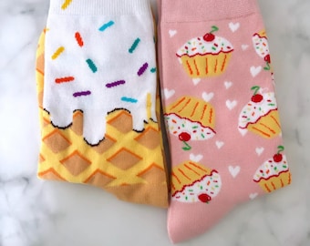 May include: A pair of colorful socks with a waffle cone and ice cream design on one sock and a cupcake design on the other sock.