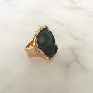 May include: A gold ring with a black oval-shaped stone set in a textured gold frame.