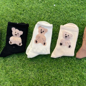 May include: Five pairs of socks with a teddy bear design. The socks are in different colors: gray, black, white, cream, and brown.