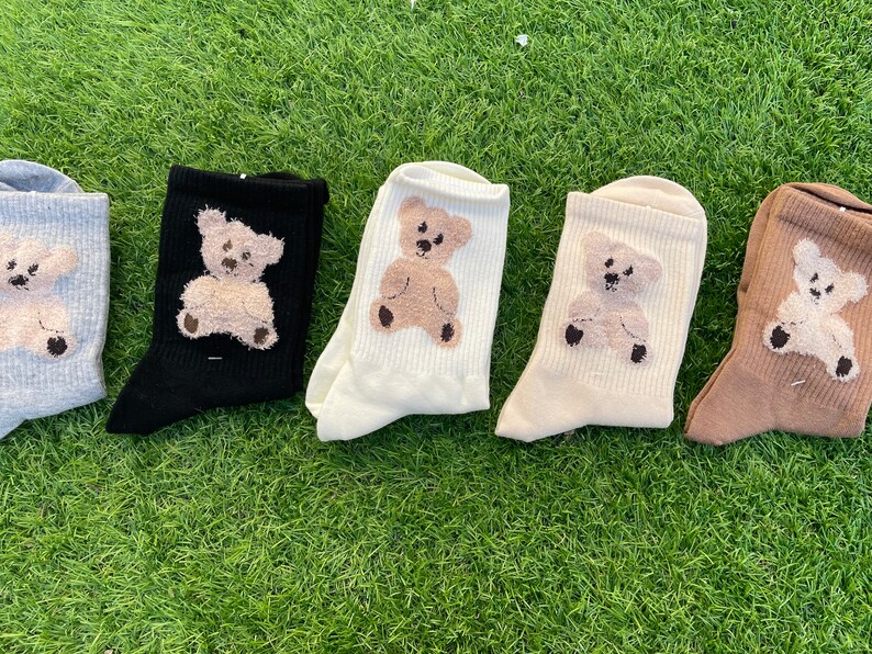 May include: Five pairs of socks with a teddy bear design. The socks are in different colors: gray, black, white, cream, and brown.