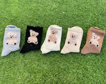 May include: Five pairs of socks with a brown teddy bear design. The socks are in different colors: gray, black, white, beige, and brown.