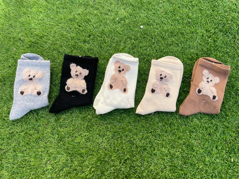 May include: Five pairs of socks with a brown teddy bear design. The socks are in different colors: gray, black, white, beige, and brown.