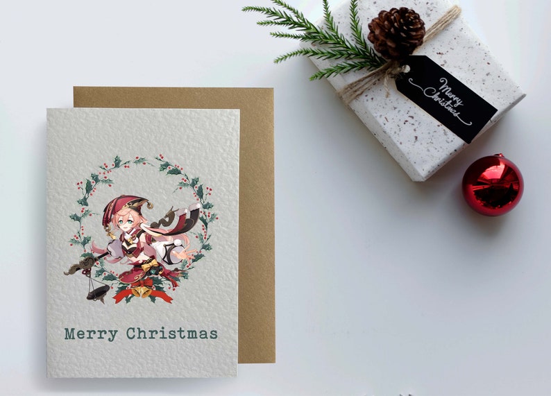 May include: A Christmas card featuring an anime character in a red and white outfit with a wreath of holly and berries around her. The card has the text "Merry Christmas" at the bottom.