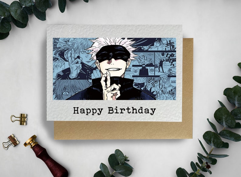May include: A birthday card featuring a black and white illustration of a character from a manga series. The character has white hair and is wearing a black shirt and a blindfold. The card has the text "Happy Birthday" printed on it.