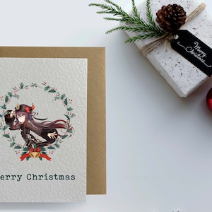 May include: A Christmas card featuring an anime-style illustration of a woman in a black and red outfit with a wreath of holly and berries around her. The text "Merry Christmas" is printed below the illustration.
