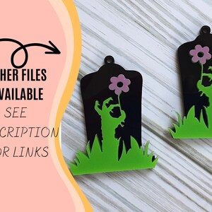 Puede incluir: Dos decoraciones de Halloween con forma de l&aacute;pida negra con una mano de zombi sosteniendo una flor rosa. Las l&aacute;pidas tienen hierba verde en la base. El texto "OTHER FILES AVAILABLE SEE DESCRIPTION FOR LINKS" est&aacute; a la izquierda.