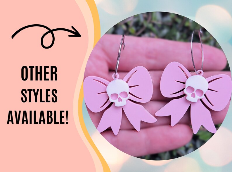 Puede incluir: Pendientes de lazo rosa con un dije de calavera blanca. Los pendientes cuelgan de aros plateados. La imagen tambi&eacute;n incluye el texto "OTHER STYLES AVAILABLE!" en letras negras.