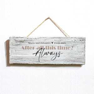Könnte beinhalten: Ein rustikales Holzschild mit weißer Bemalung, das an einem Bindfaden hängt. Das Schild zeigt den Text "After all this time! Always" in schwarzer Schrift, mit den Worten "Maria und Johannes ♥ 24.08.2023" in hellrosa darüber.