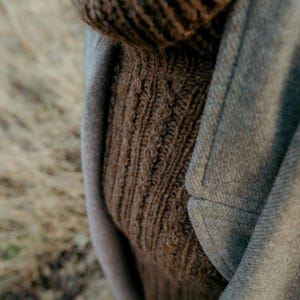 Peut inclure: Un pull en tricot torsadé marron porté sous un manteau en laine gris.