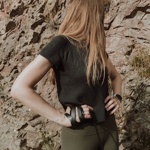 May include: A person wearing a black shirt and olive green leggings, holding a black leash.