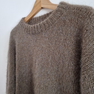 May include: A brown fuzzy sweater hanging on a wooden hanger. The sweater is made of a soft, knitted fabric.