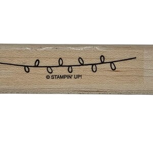 May include: Wooden stamp featuring a string of black lights. The stamp has the text "STAMPIN' UP!" printed on the wood. The stamp is rectangular and made of light-colored wood.