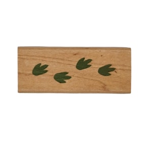 May include: A wooden block with five green dinosaur footprints painted on it.