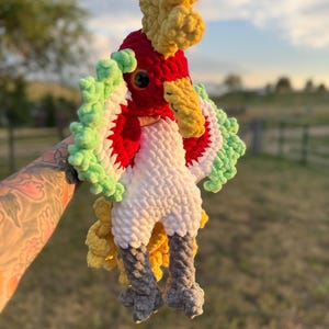 May include: A handmade crochet parrot in vibrant colors. The bird features a red head, white body, and green and white wings. The parrot has yellow accents on its crest and beak, and gray legs. A unique, soft, and colorful plush toy.
