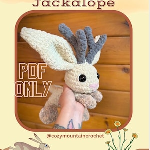 Pu&ograve; includere: Un peluche di jackalope all'uncinetto con grandi orecchie e corna grigie. Il jackalope &egrave; color crema con occhi neri e naso rosa. Il testo "Juniper the Jackalope" e "PDF ONLY" sono visualizzati. L'immagine include anche un'illustrazione di lepre in corsa.