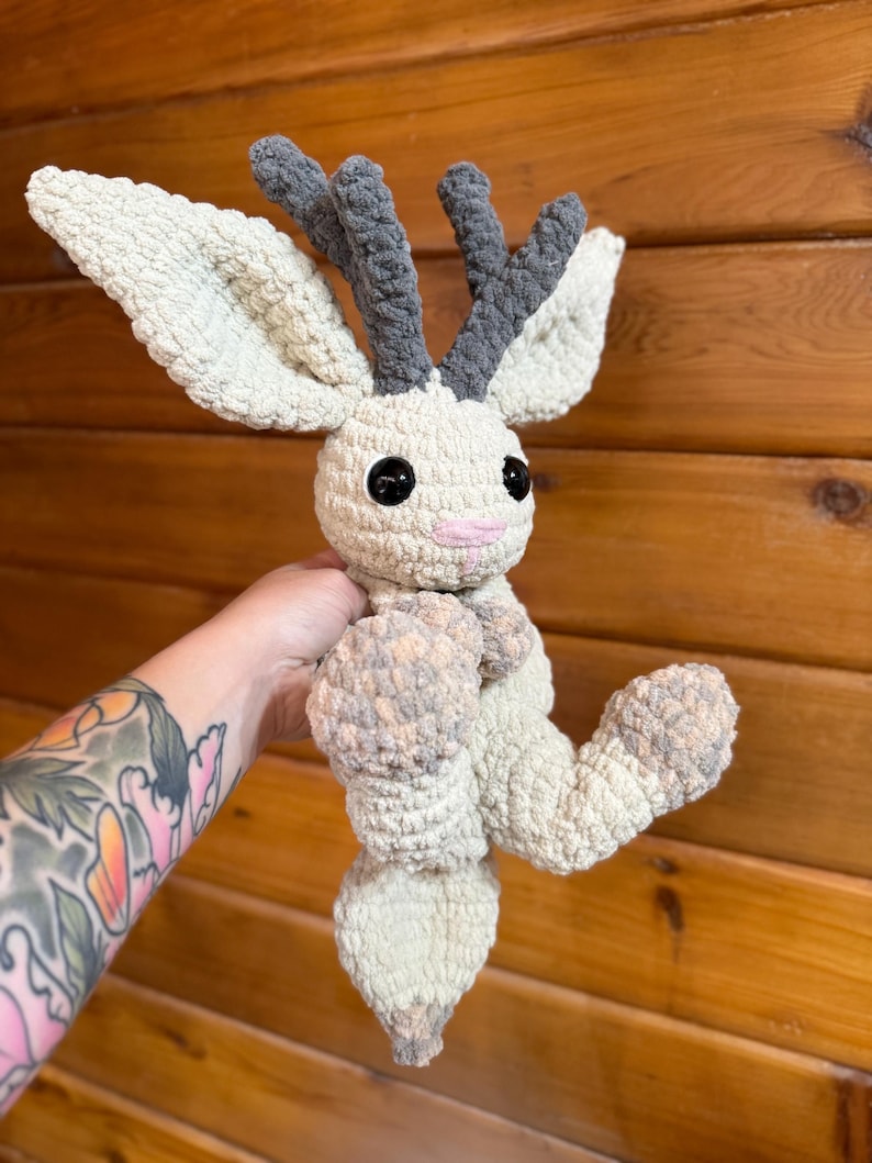 Pu&ograve; includere: Un peluche all'uncinetto fatto a mano a forma di creatura mitica. Il peluche ha grandi orecchie color crema, corna grigie e occhi neri. Il corpo &egrave; color crema e grigio, con una bocca rosa. Il giocattolo &egrave; morbido e strutturato.