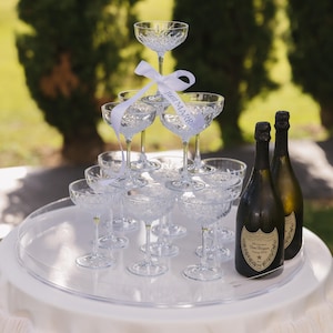 May include: A champagne tower made of crystal champagne flutes with a white ribbon that says "Just Married" and two bottles of Dom P&eacute;rignon champagne on a white round table.