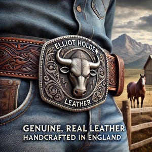 May include: A silver belt buckle with a bull's head design and the text "Elliot Holden Leather" on a brown leather belt. The belt is worn by a person wearing blue jeans. The background shows a mountain range and a wooden fence.