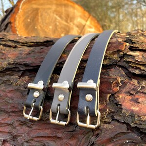 May include: Three leather belts with silver buckles. The belts are arranged in a row, with the black belt on the right, the gray belt in the middle, and the brown belt on the left.
