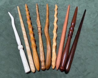 May include: A collection of eight handcrafted wooden wands in various shades of brown, tan, and white. The wands feature diverse textures, including smooth, tapered, spiraled, and carved surfaces, showcasing natural wood grain patterns and finishes.
