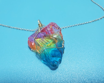 May include: A rainbow crystal pendant necklace with a gold wire wrap. The crystal is a rough, irregular shape and has a variety of colors, including red, orange, yellow, green, blue, and purple.