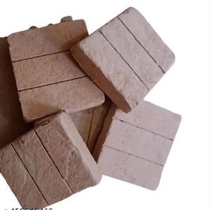 May include: A collection of square, light brown coasters with a textured, brick-like appearance. Each coaster has three horizontal lines etched across its surface. The coasters are stacked and slightly overlapping, creating a rustic aesthetic.