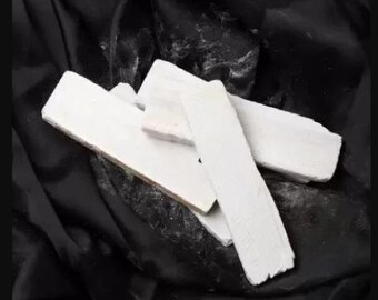May include: Several rectangular white chalk pieces are arranged on a black, textured surface. The chalk appears to have a slightly rough texture and varying thicknesses, suggesting a natural or handmade quality. The image is well-lit, highlighting the chalk's color.