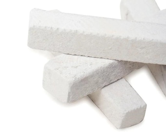May include: A collection of white, rectangular chalk pieces with textured surfaces. The chalk sticks are stacked and angled against each other, creating a layered effect. The image is set against a white background.