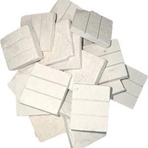 May include: A pile of off-white, square-shaped coasters. Each coaster has three horizontal lines etched across its surface. The coasters are made of a textured material and are arranged in a random, overlapping pattern.