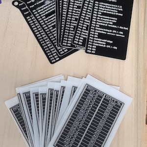 May include: A collection of black rectangular plastic tags featuring white printed instructions for programming settings, alongside a stack of white rectangular stickers displaying a 60V 16S battery percentage voltage chart with numerical data.