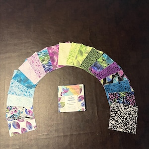 May include: A stack of fabric squares labelled Maple Squares with a rainbow bird logo, surrounded by an arc of individual fabric swatches featuring various patterns in blue, purple, green, black, and white, all with pinked edges.
